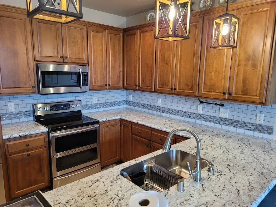 Kitchen with wood cabinets, white countertops, stainless steel appliances, and hanging light fixtures.