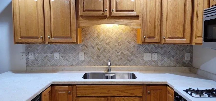 Kitchen with light wood cabinets, white countertops, and patterned backsplash. Stainless steel sink.