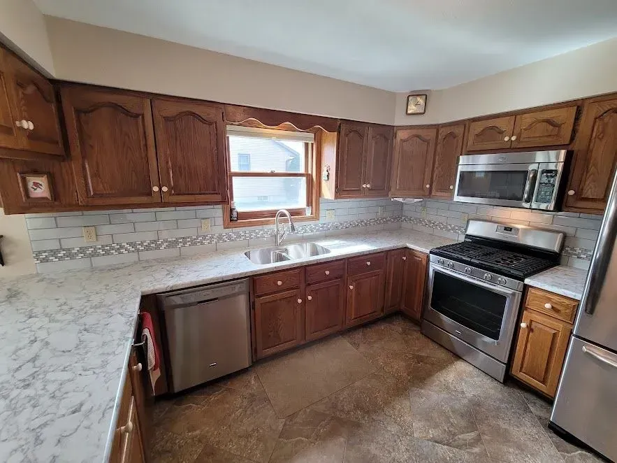Kitchen with dark wood cabinets, stainless steel appliances, white countertops, and patterned backsplash.