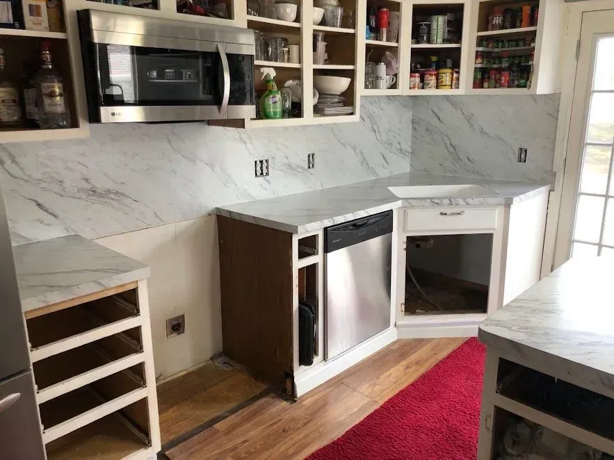 Kitchen under construction with white cabinets, marble countertops, stainless steel appliances.