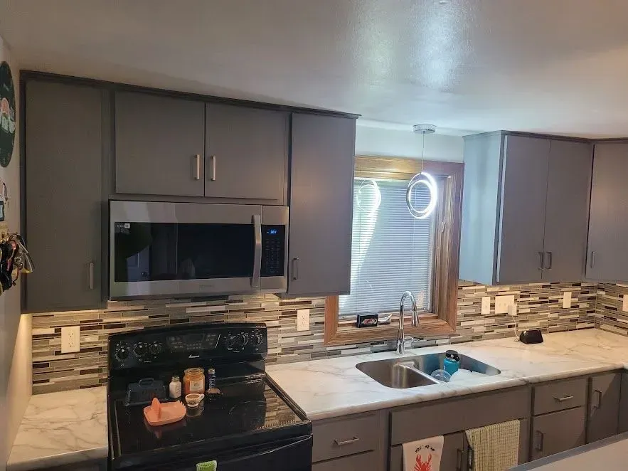 Gray kitchen with microwave, stove, cabinets, and a window with blinds.