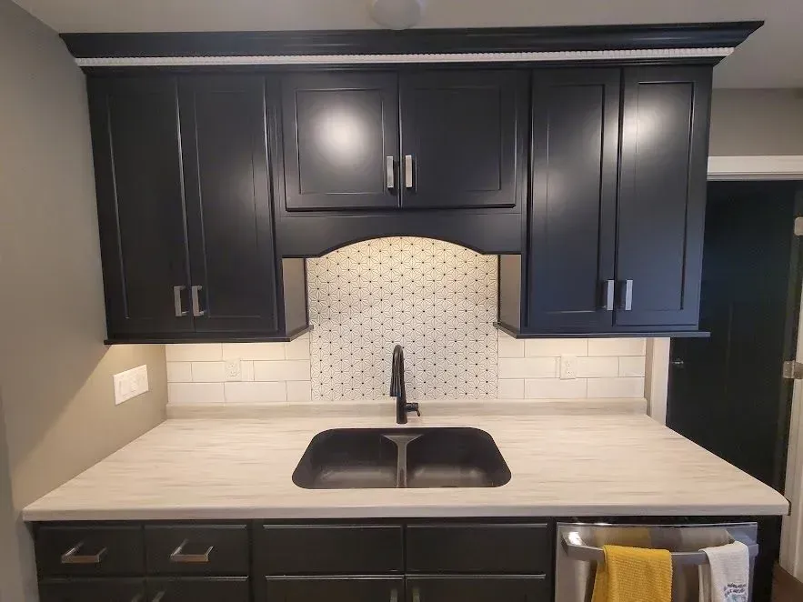 Black kitchen cabinets with a white countertop and backsplash, above a sink and lower cabinets.