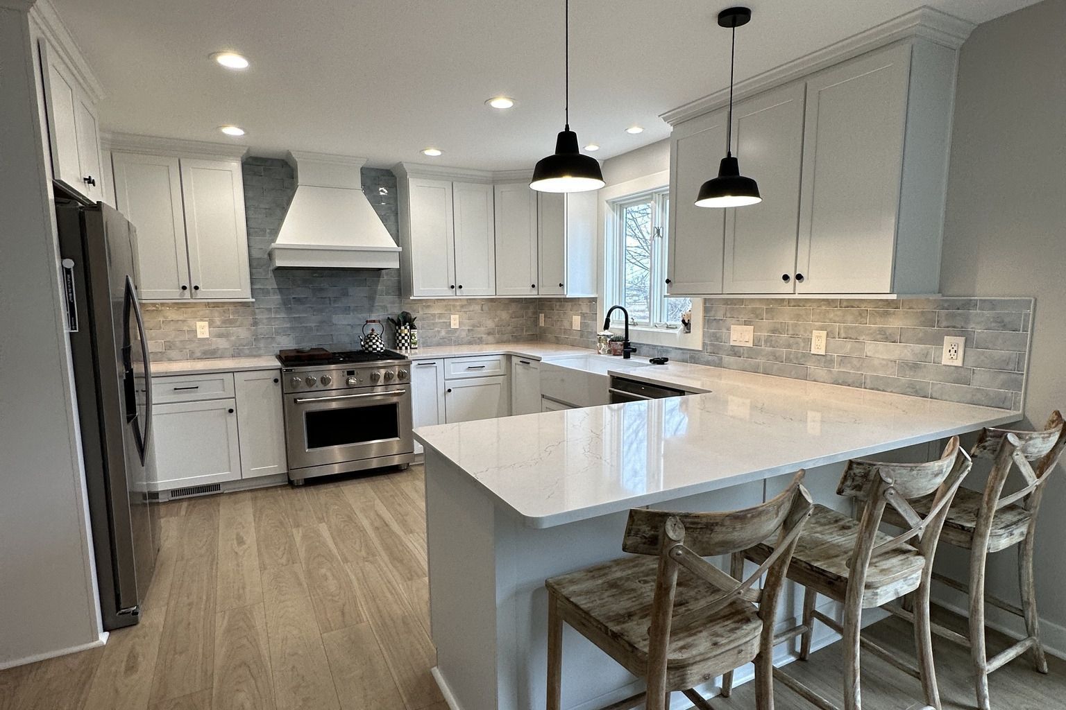 Modern white kitchen with stainless steel appliances, light wood floors, and three bar stools.