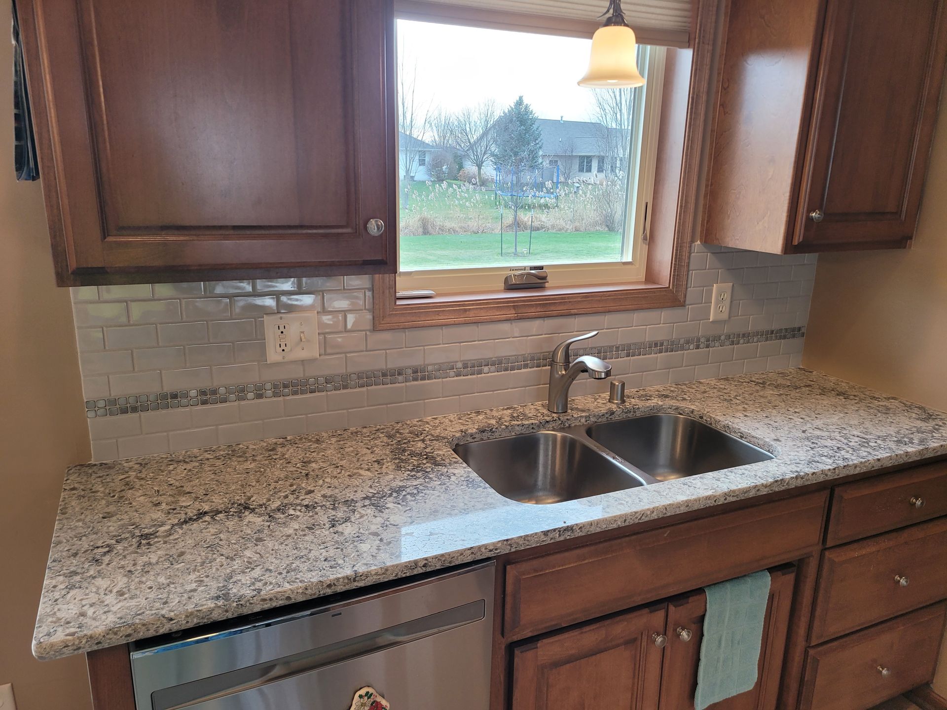 Kitchen with granite countertops, stainless steel sink, tile backsplash, and wooden cabinets.