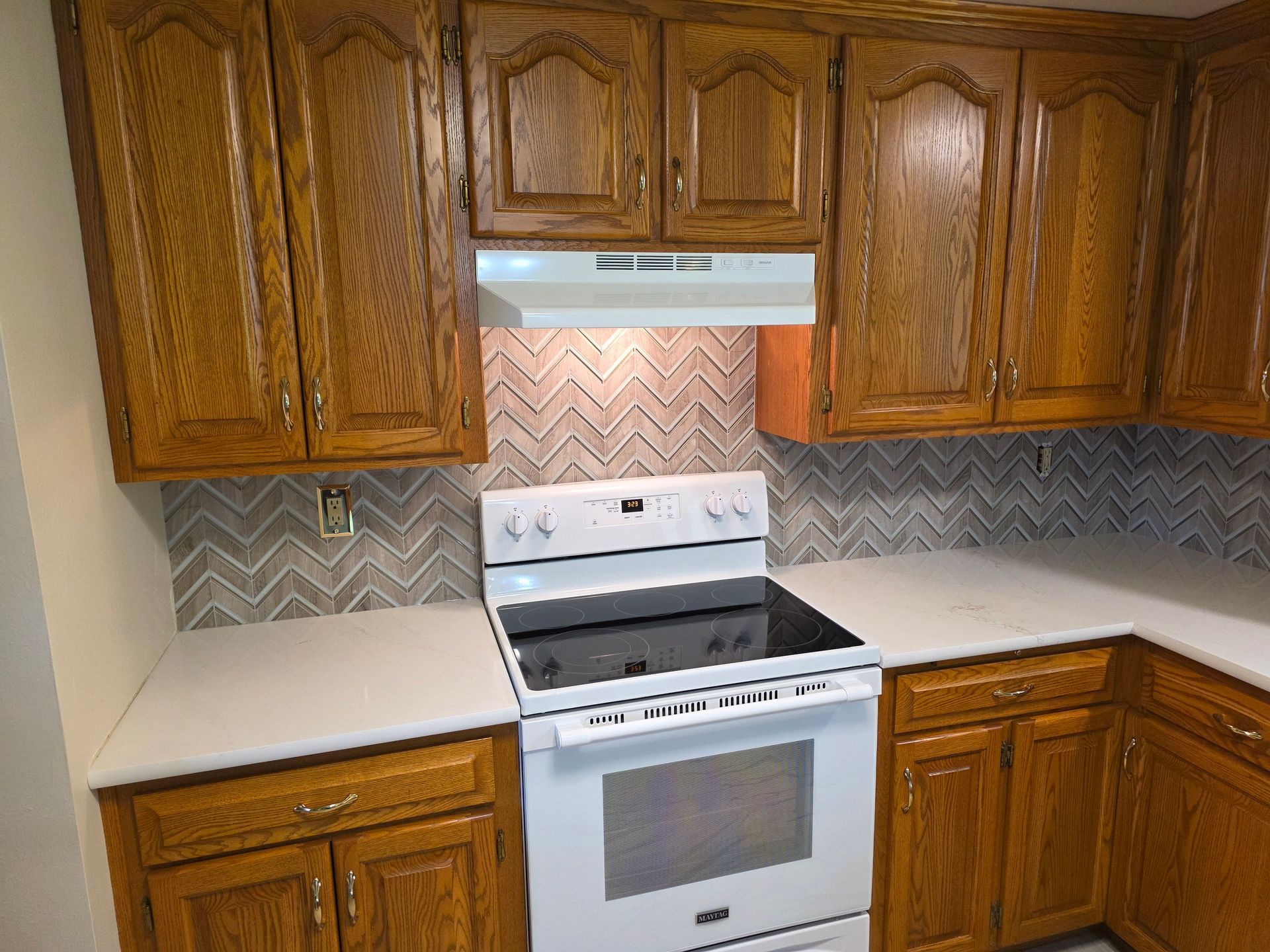 Kitchen with brown cabinets, white stove, and gray patterned backsplash.
