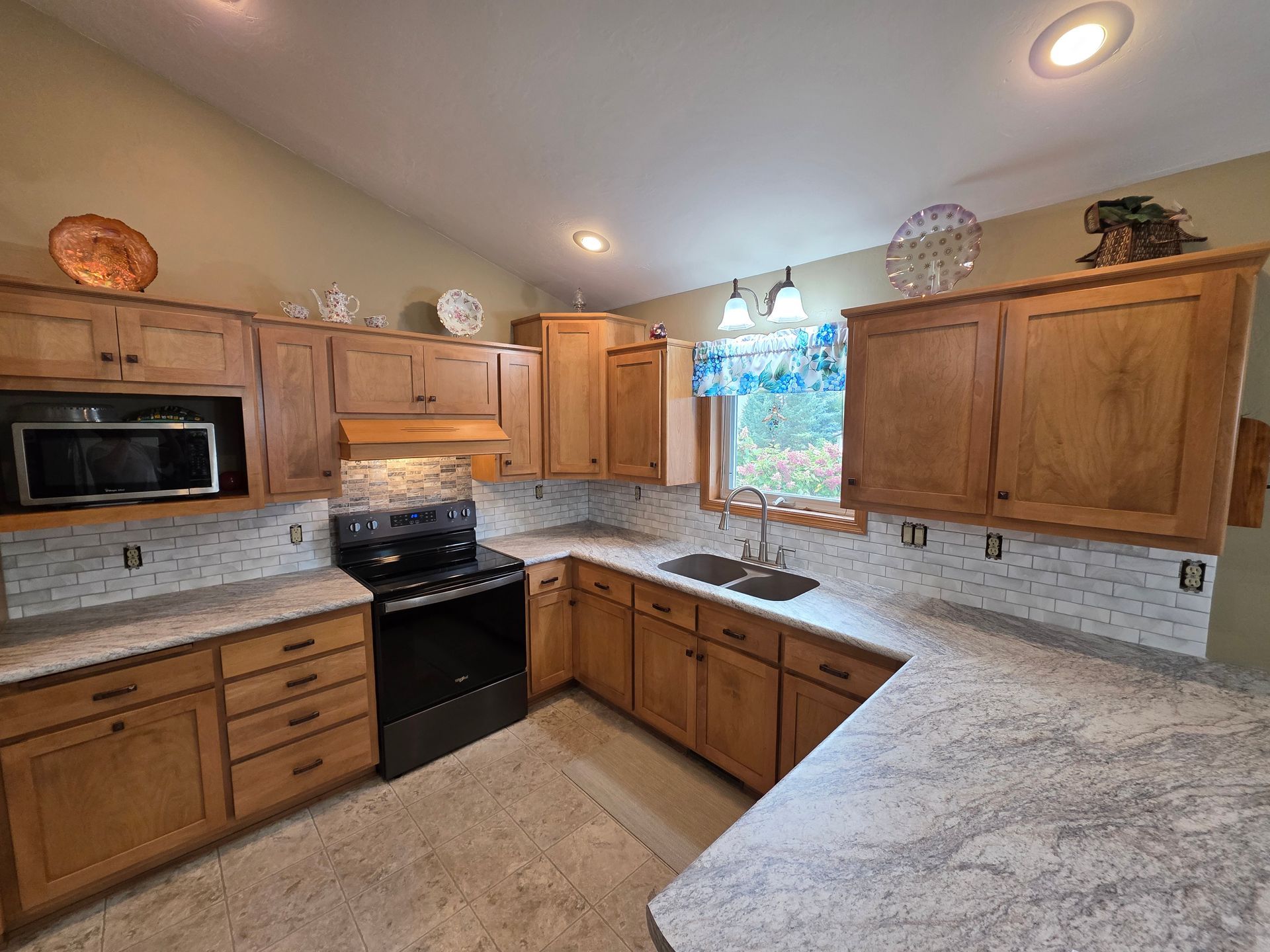Kitchen with light wood cabinets, granite countertops, and black appliances.