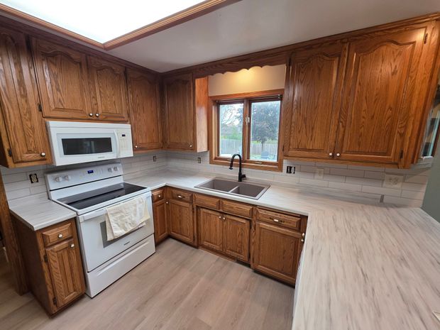 Kitchen with wooden cabinets, white appliances, and light countertops. A window is above the sink.