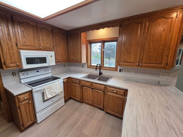 Kitchen with wooden cabinets, white appliances, and light countertops. A window is above the sink.