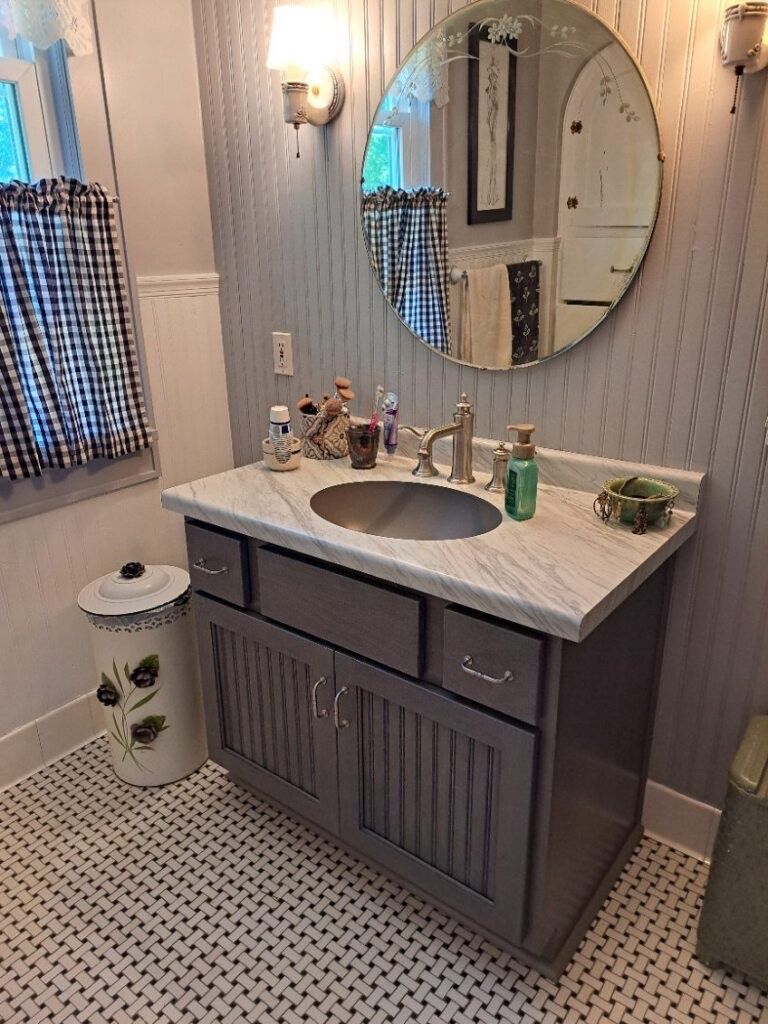 Bathroom with gray vanity, round mirror, and checkered curtains.
