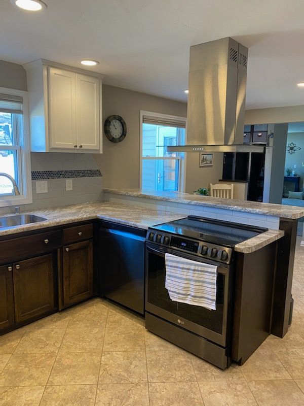Kitchen with dark cabinets, gray countertops, stainless steel range hood, and beige tile floor.