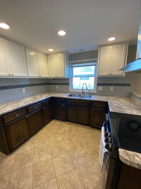 Kitchen with brown and white cabinets, tan tile floor, and a window above the sink.