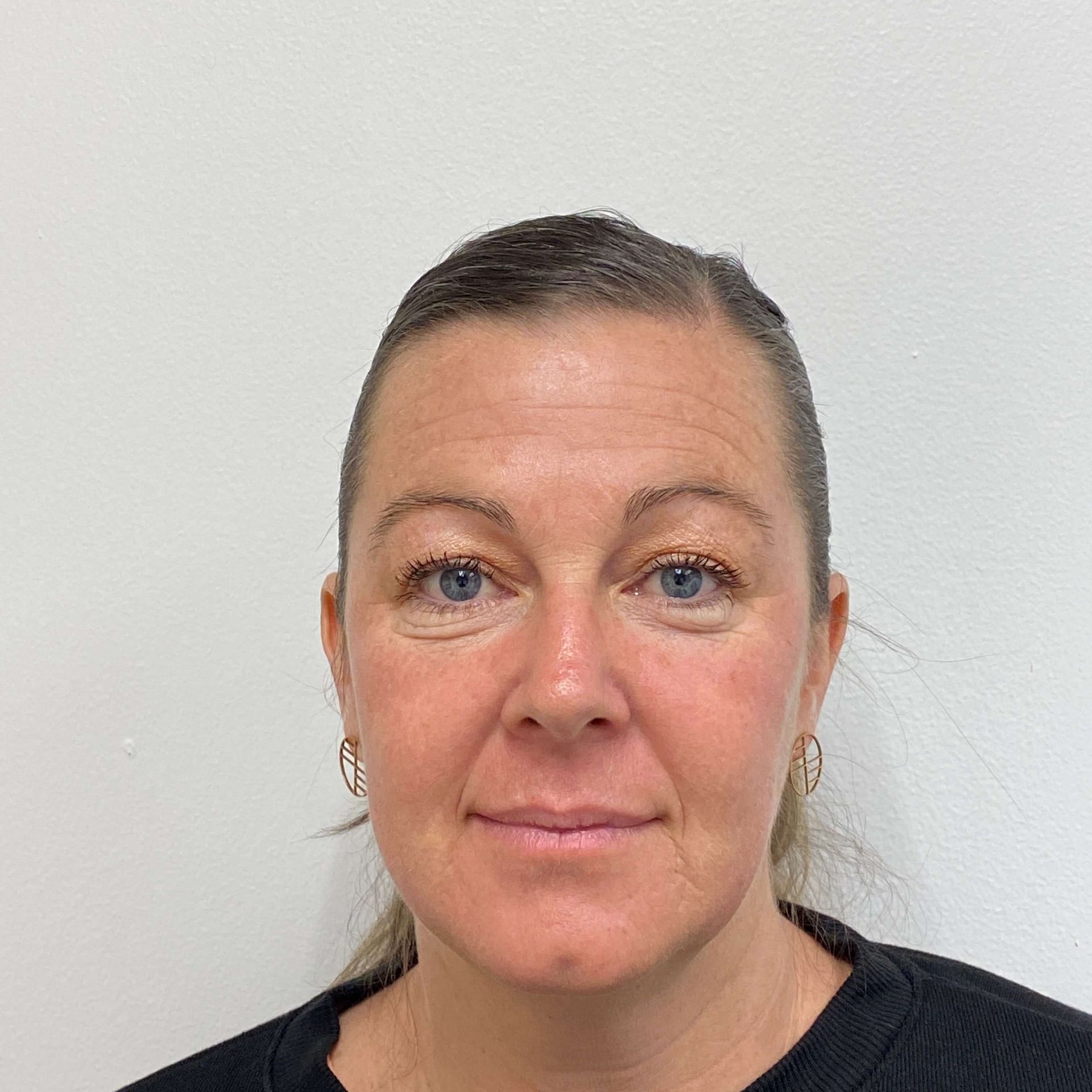 A person with pulled-back hair and gold hoop earrings posing against a plain, light-colored background.