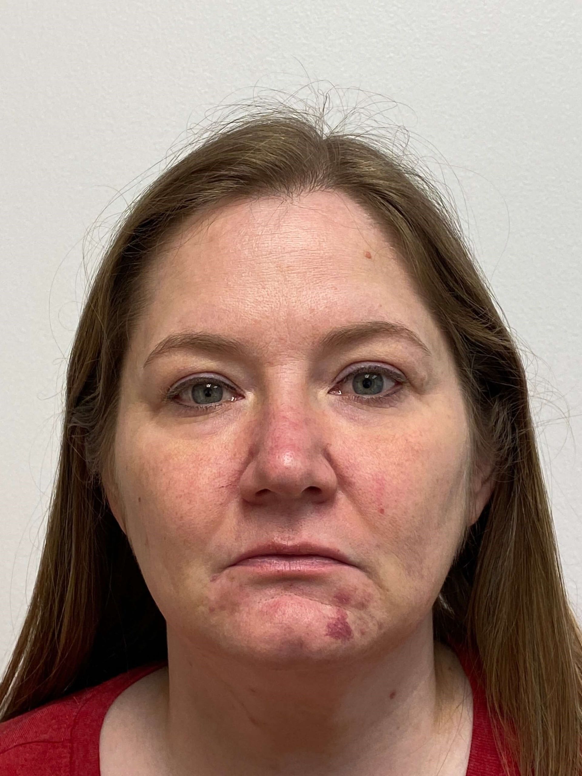 A head-and-shoulders portrait of a person with long brown hair, wearing a red shirt against a plain white background.