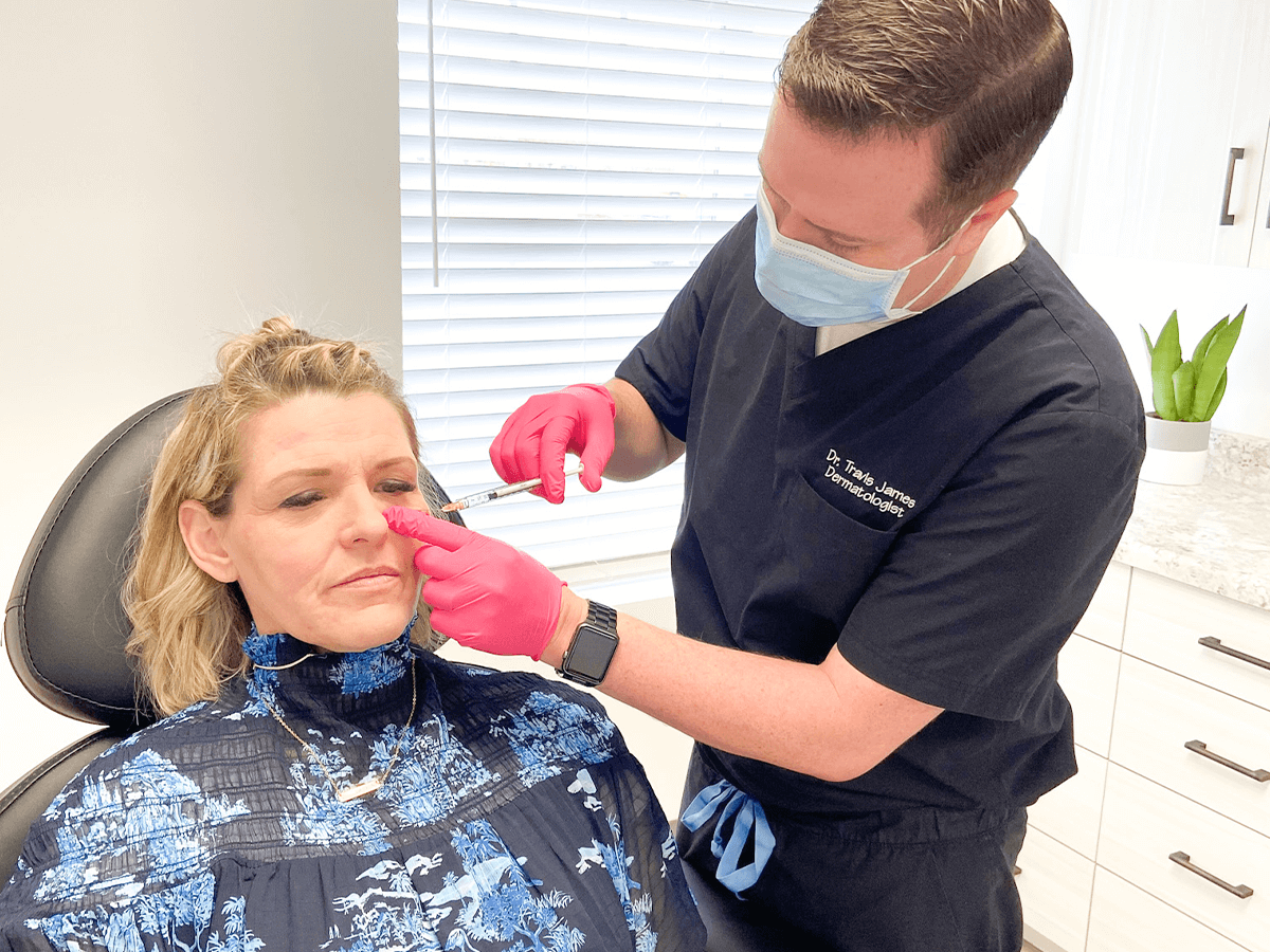 A professional administering a facial filler injection to a patient's under-eye area in a clinical setting.