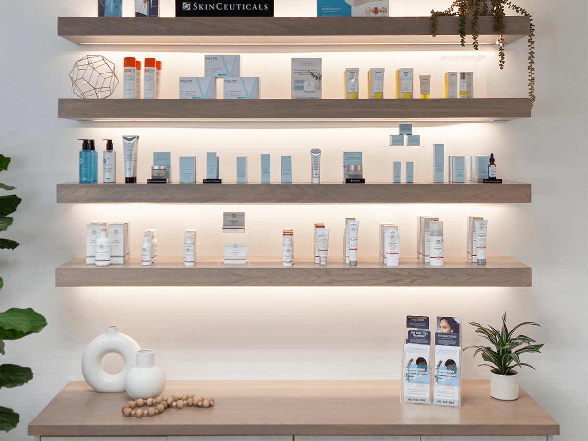 Light-colored wooden shelves displaying various skincare products in bottles and boxes against a white wall.