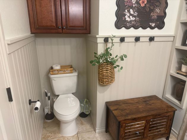 Small bathroom with toilet, wood cabinet, woven plant basket, and rustic storage bench.