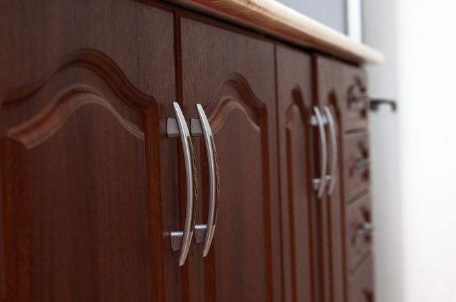 Wooden cabinet with curved silver handles in a bright room.