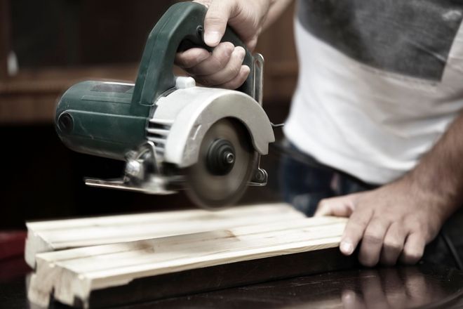 Person using a circular saw to cut a wooden plank on a workbench.