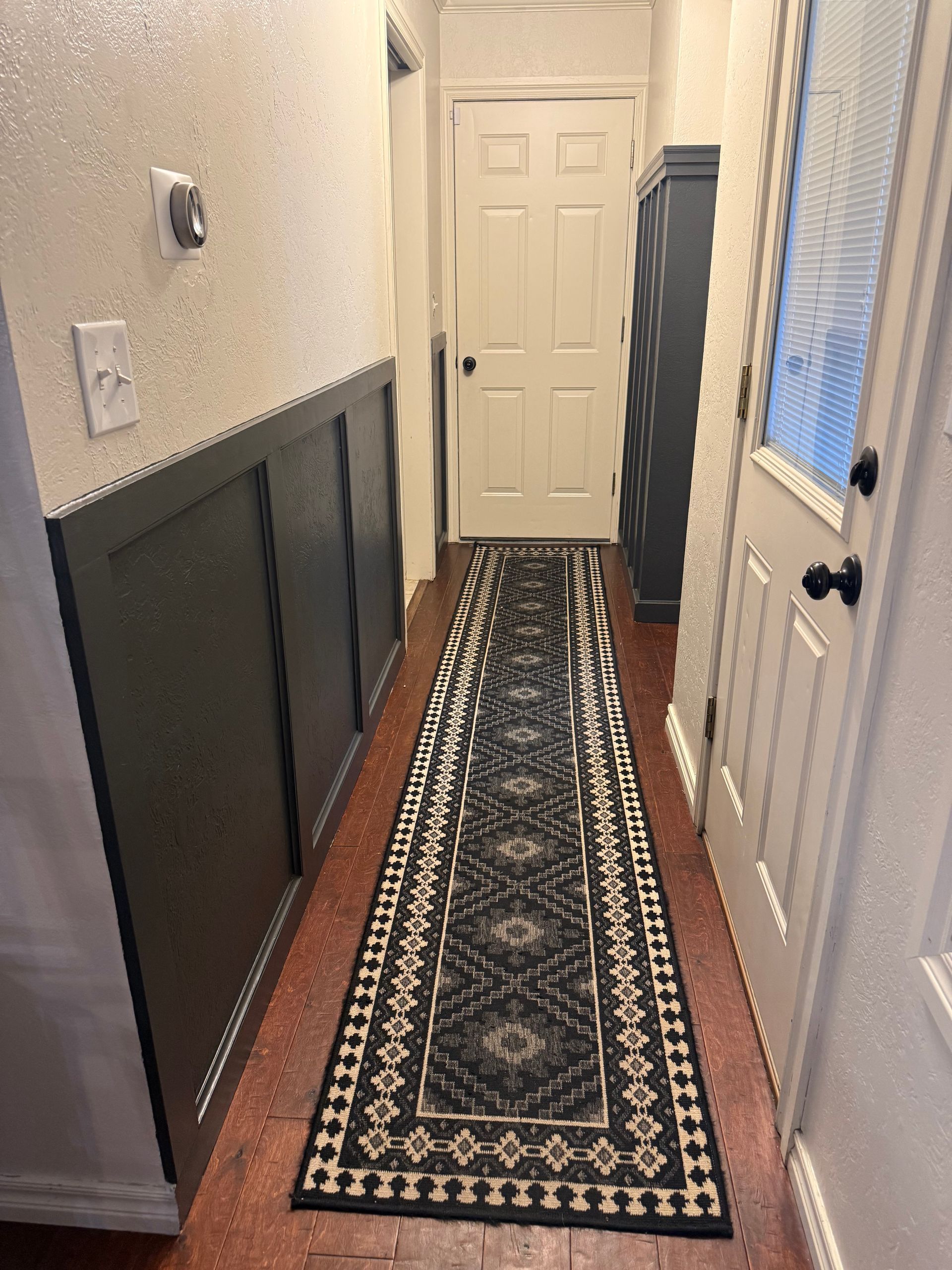 Narrow hallway with patterned runner rug, white doors, and dark wall paneling.