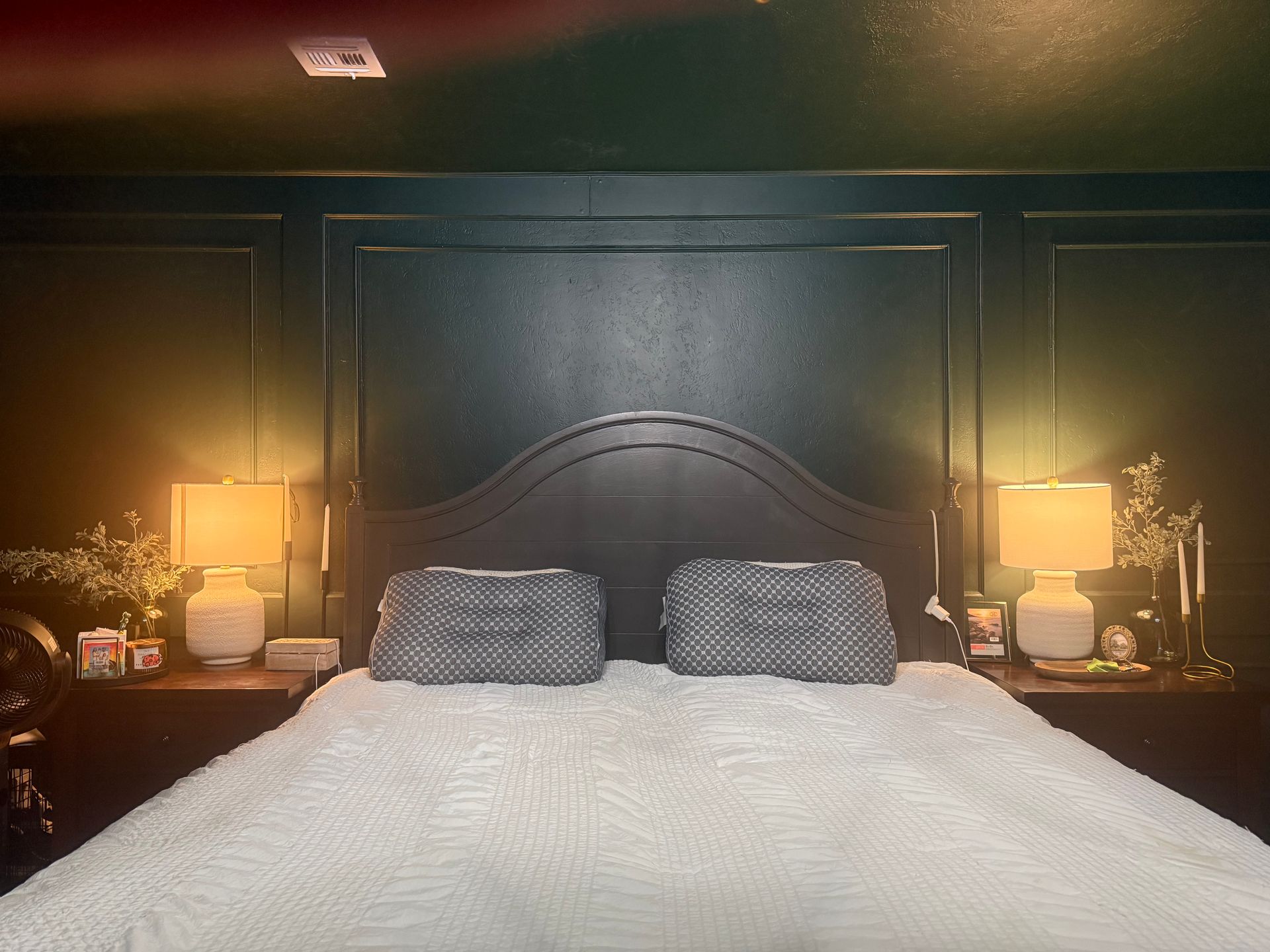Dark bedroom with a black headboard, white bedspread, and warm bedside lamps on both sides.