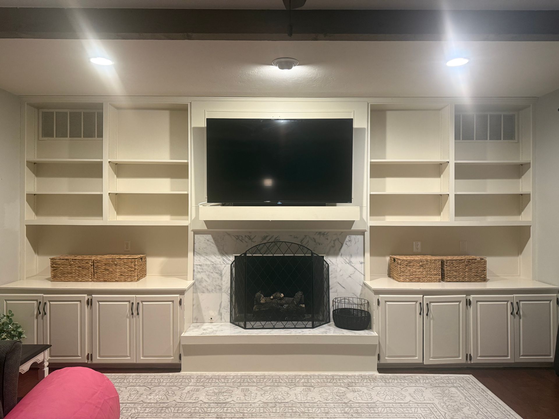 Built-in living room fireplace with TV, white cabinets, shelves, and pink chairs on both sides.