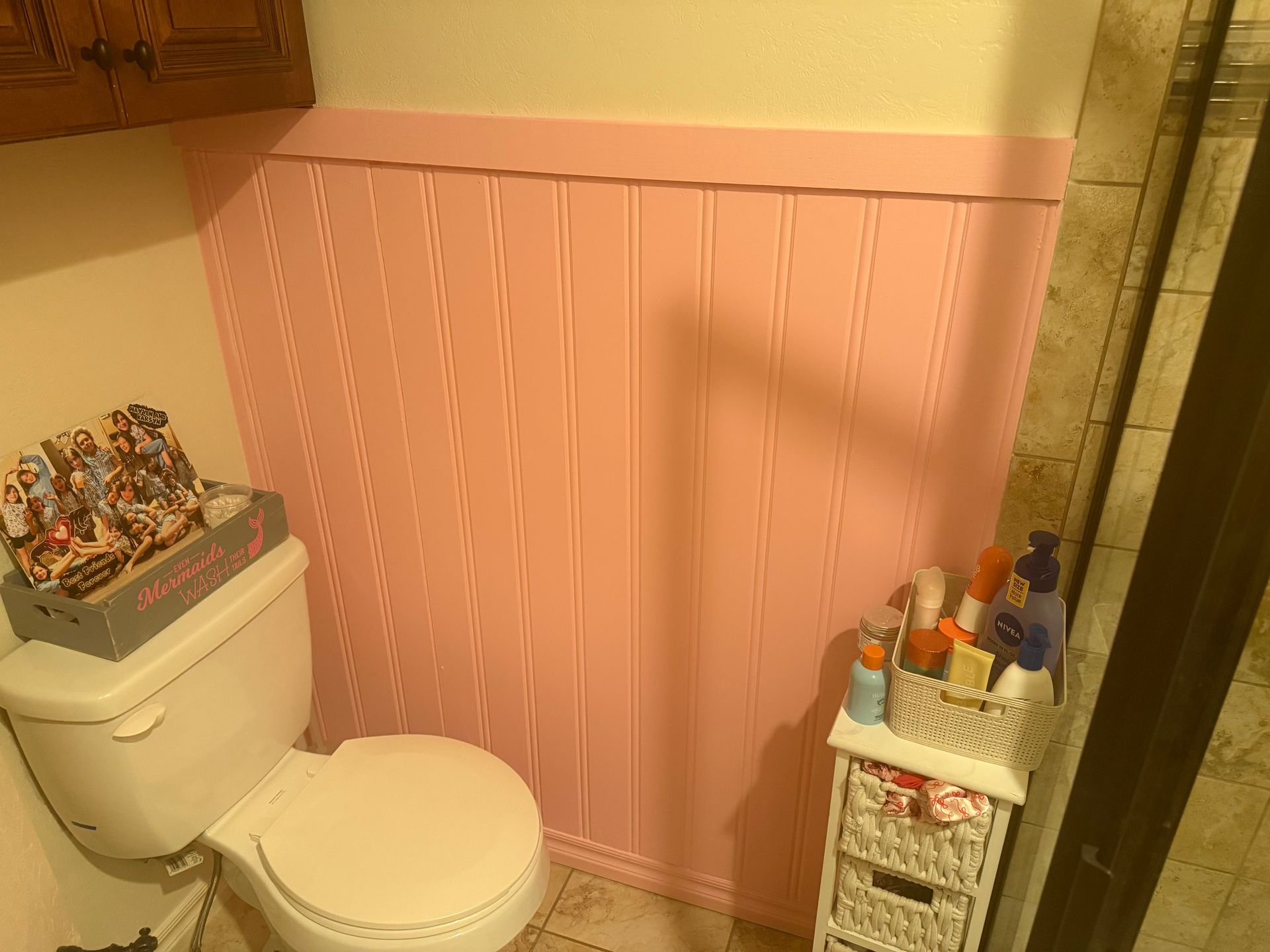 Pink wainscoted bathroom with a toilet and a small storage cart by the shower.