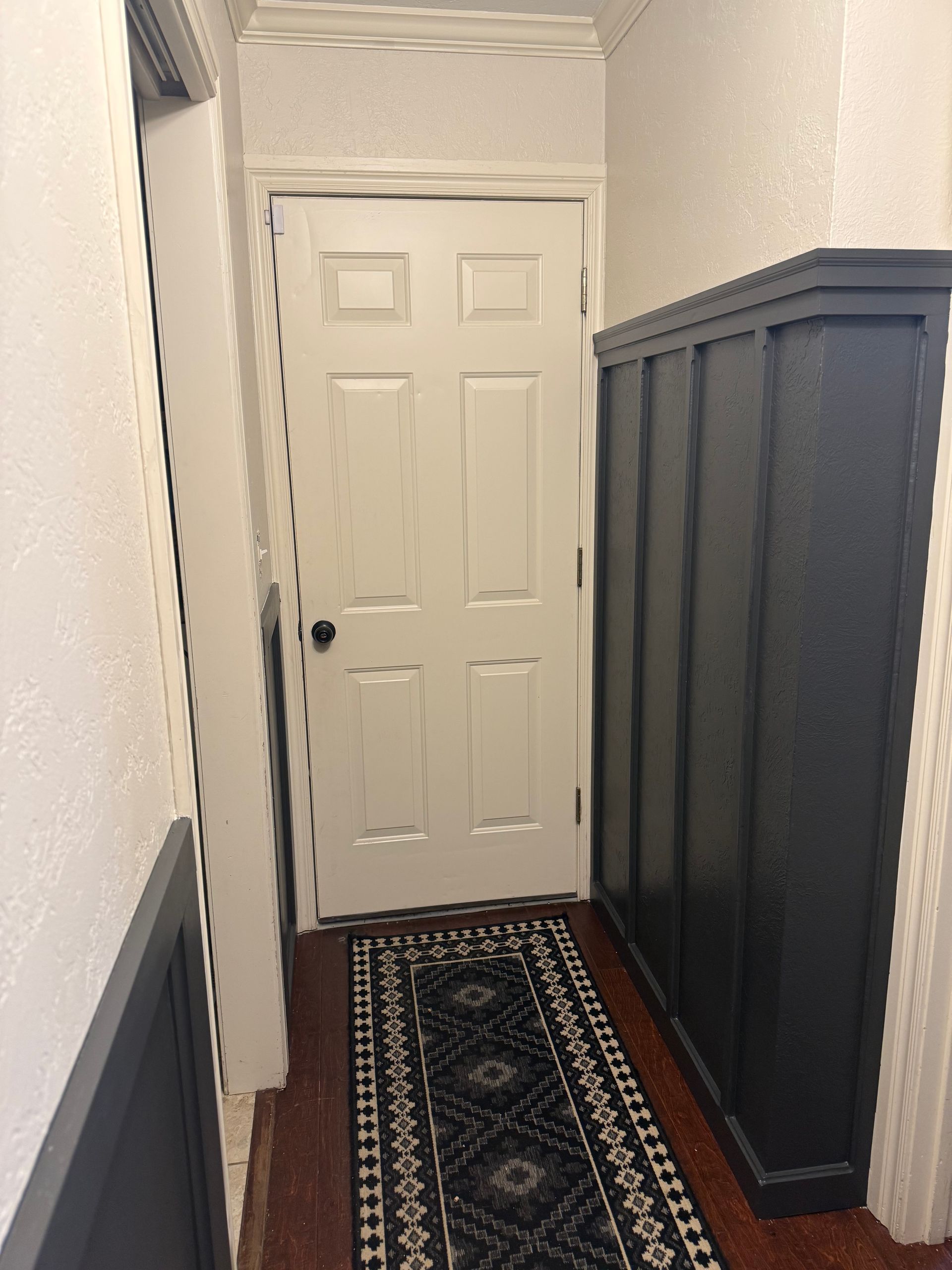 Narrow hallway with a white door, blue wainscoting, and a patterned runner rug.