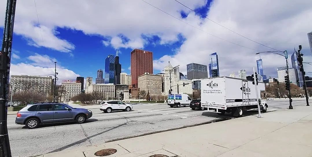 City street scene with cars and buildings under a blue sky with clouds.