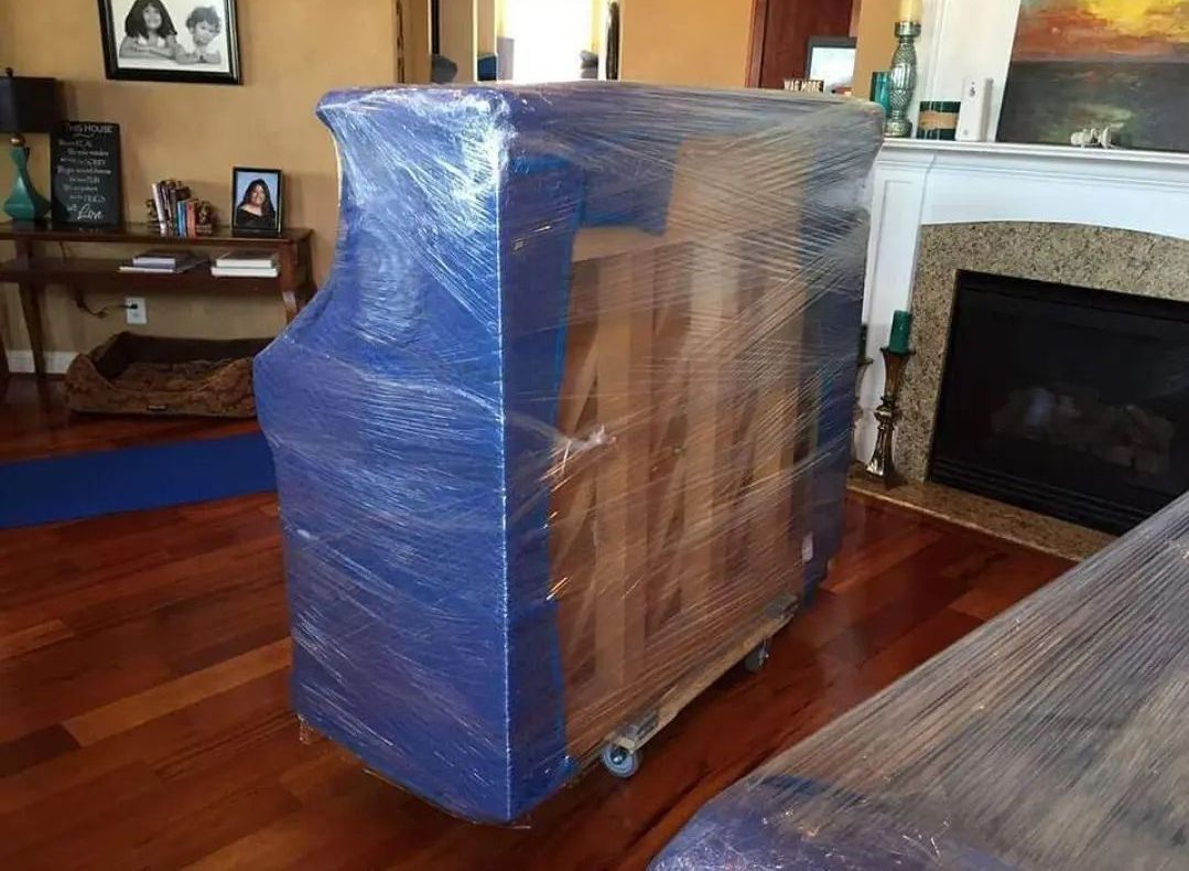 Furniture wrapped in blue plastic, on wheels, ready for transport.