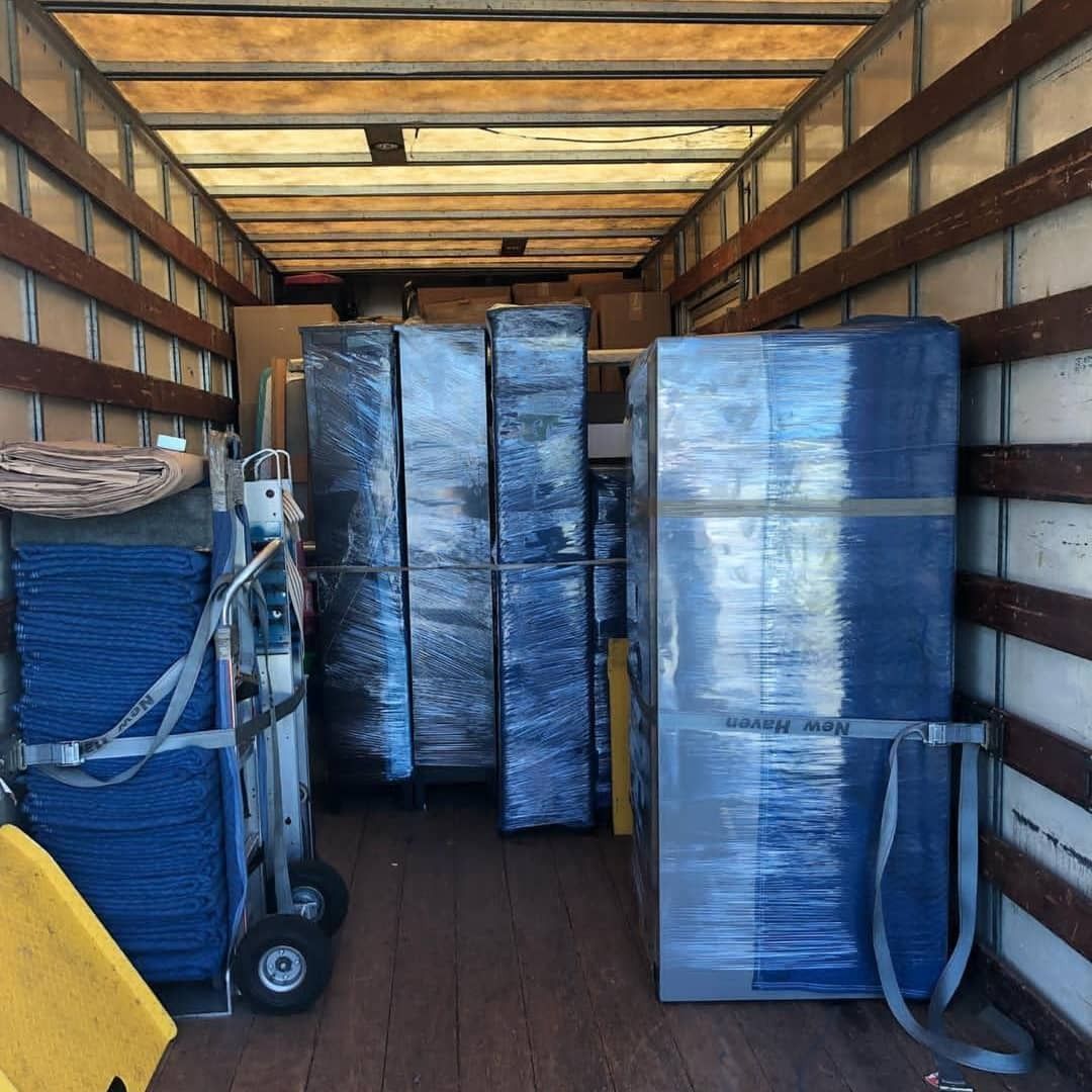 Interior of a moving truck loaded with wrapped furniture and a dolly. Wooden walls.