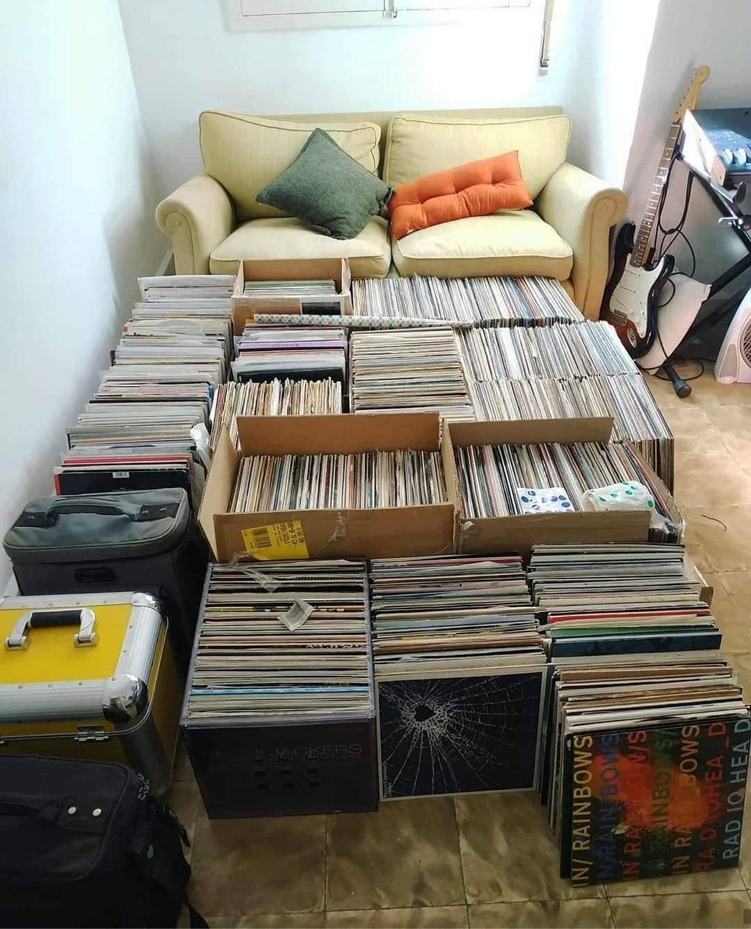 Collection of vinyl records arranged on the floor in front of a yellow couch.