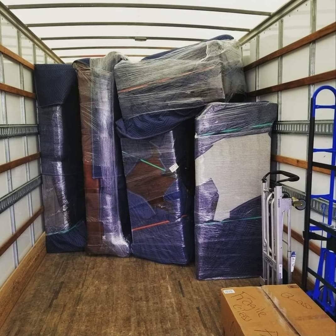 Inside of a moving truck loaded with furniture wrapped in plastic, ready for transport.