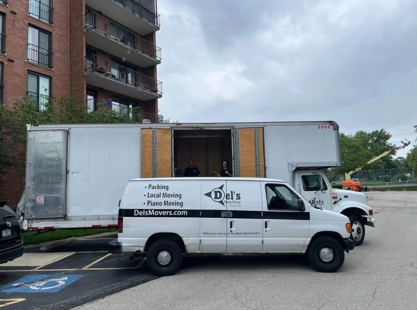White moving van and truck parked near a brick apartment building.