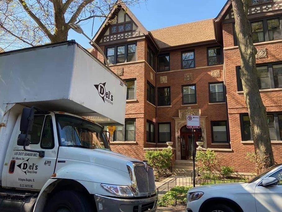 Moving truck in front of a brick apartment building with brown roof.