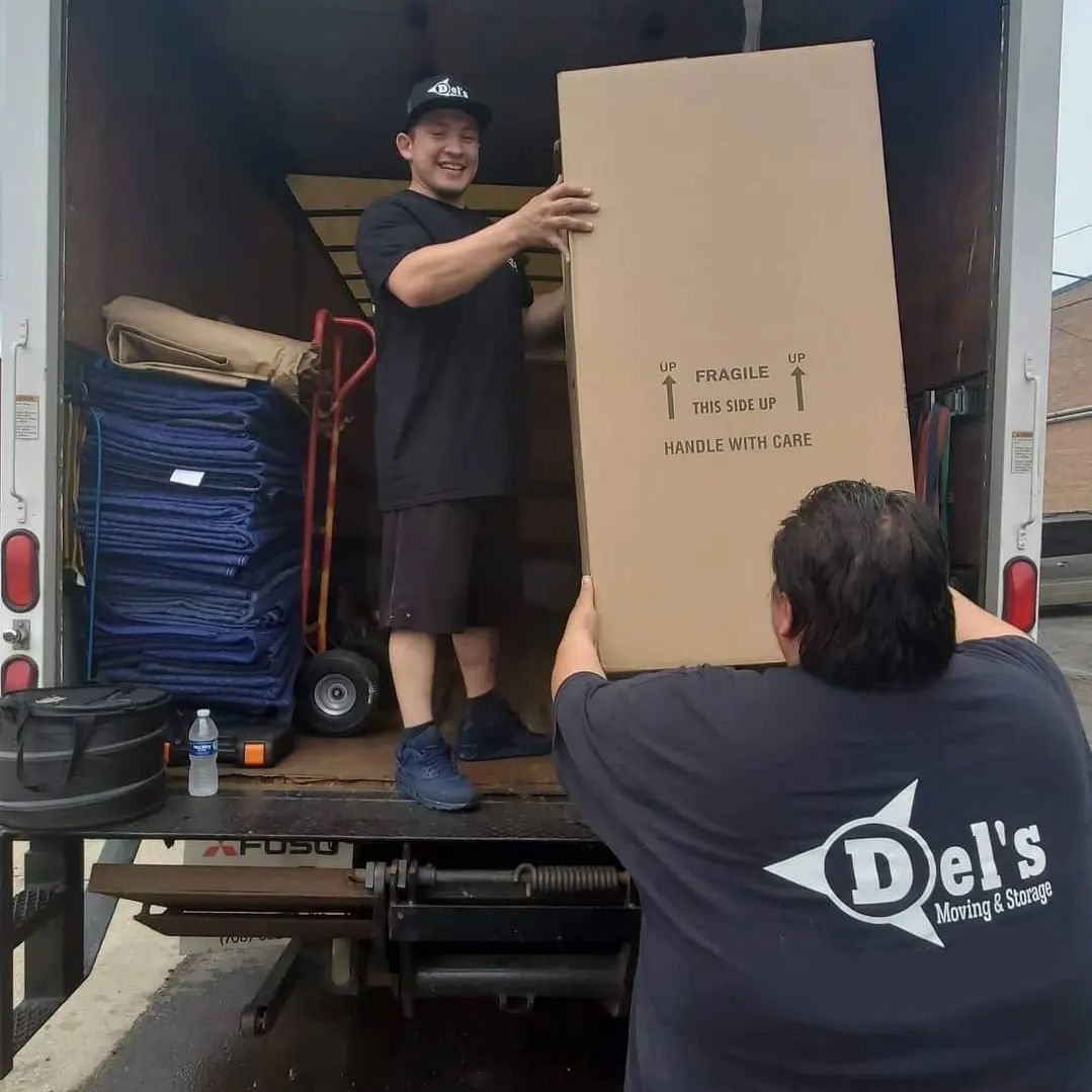 Two movers unloading a large box from a truck; one is inside the truck, one is on the ramp.