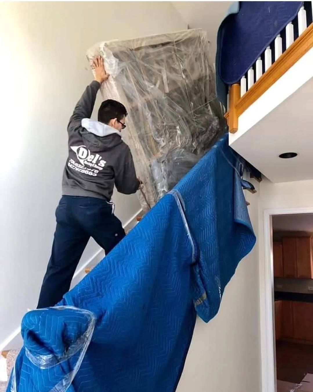 Man carrying wrapped furniture up a staircase, blue moving pads lining stairs.