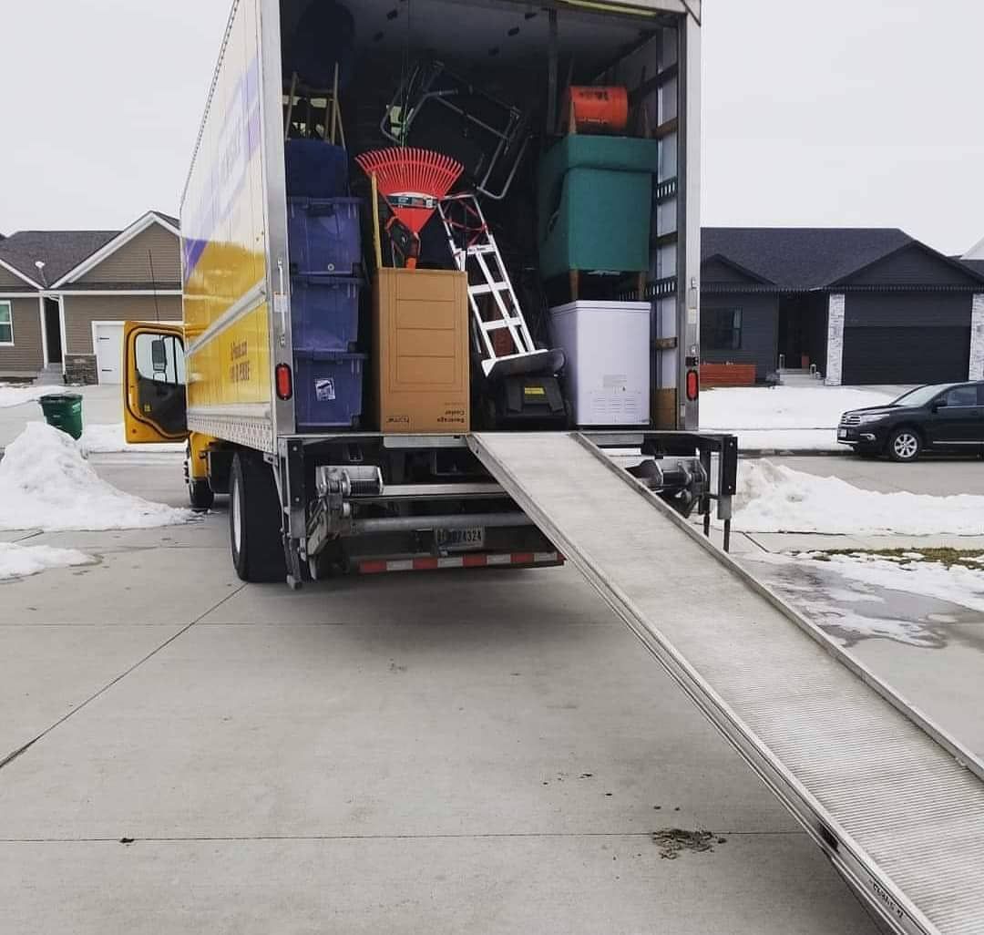 Moving truck with ramp open, filled with furniture and boxes, parked in a driveway with snow, during a move.