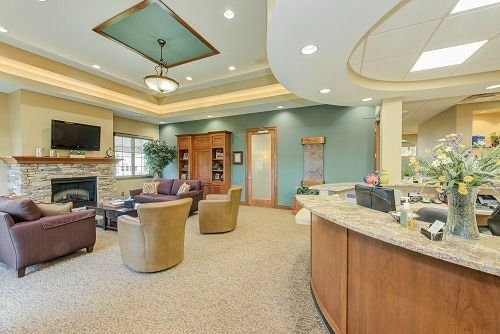 A reception area with fireplace, sofas, chairs, and front desk.  Tan carpet, teal walls and ceiling, warm lighting.