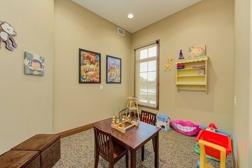 A children's play room with a table, chairs, toys, artwork, and a window.