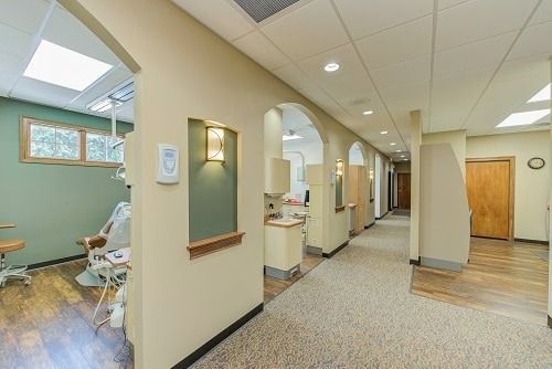 Hallway in a dental office with archways, beige walls, and carpet. Exam room is on the left.