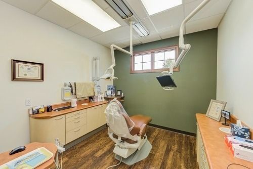 A dentist's office interior with a chair, cabinets, window, and equipment.