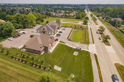 Aerial view of a building complex with parking, a playground, and a road. Green grass and trees surround the buildings.