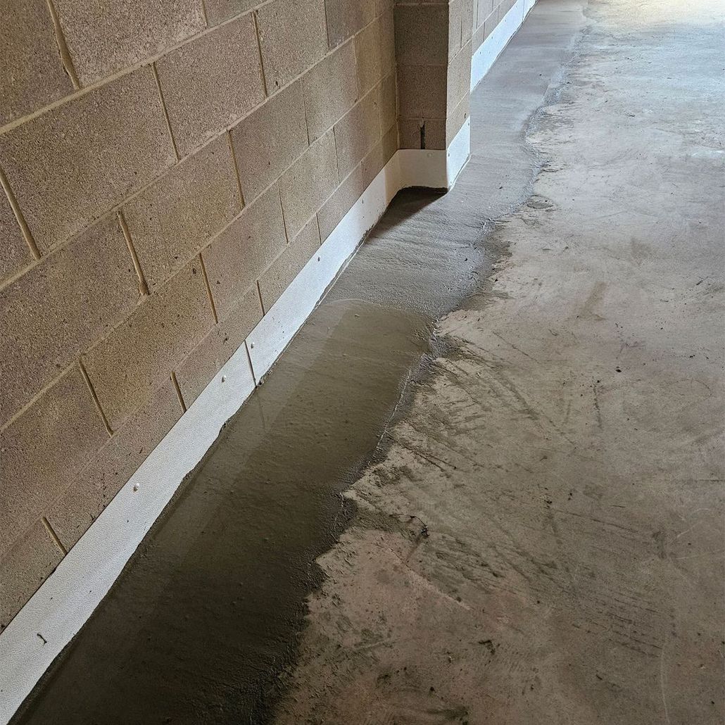 A close-up view of a newly applied concrete patch along the base of a tan brick wall and concrete floor in a garage.