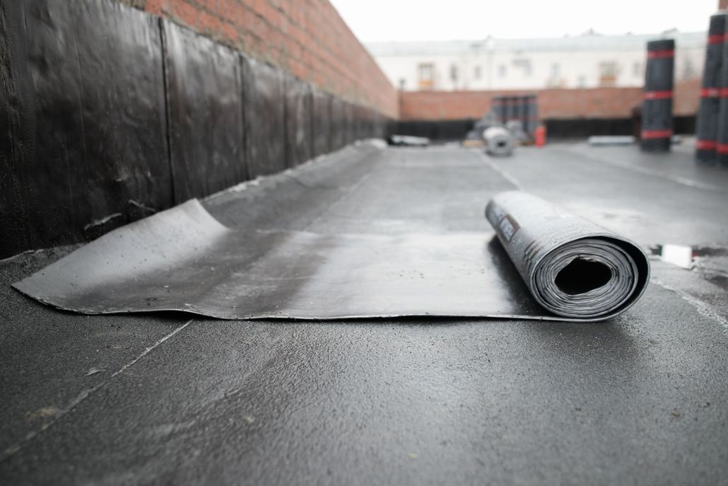 Rolled roofing membrane on a flat rooftop with a red brick parapet wall