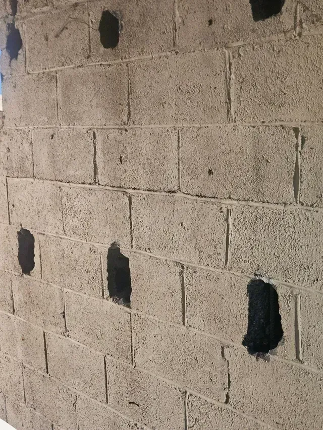 A close-up of a gray concrete block wall with several evenly spaced, dark, roughly rectangular injection holes.