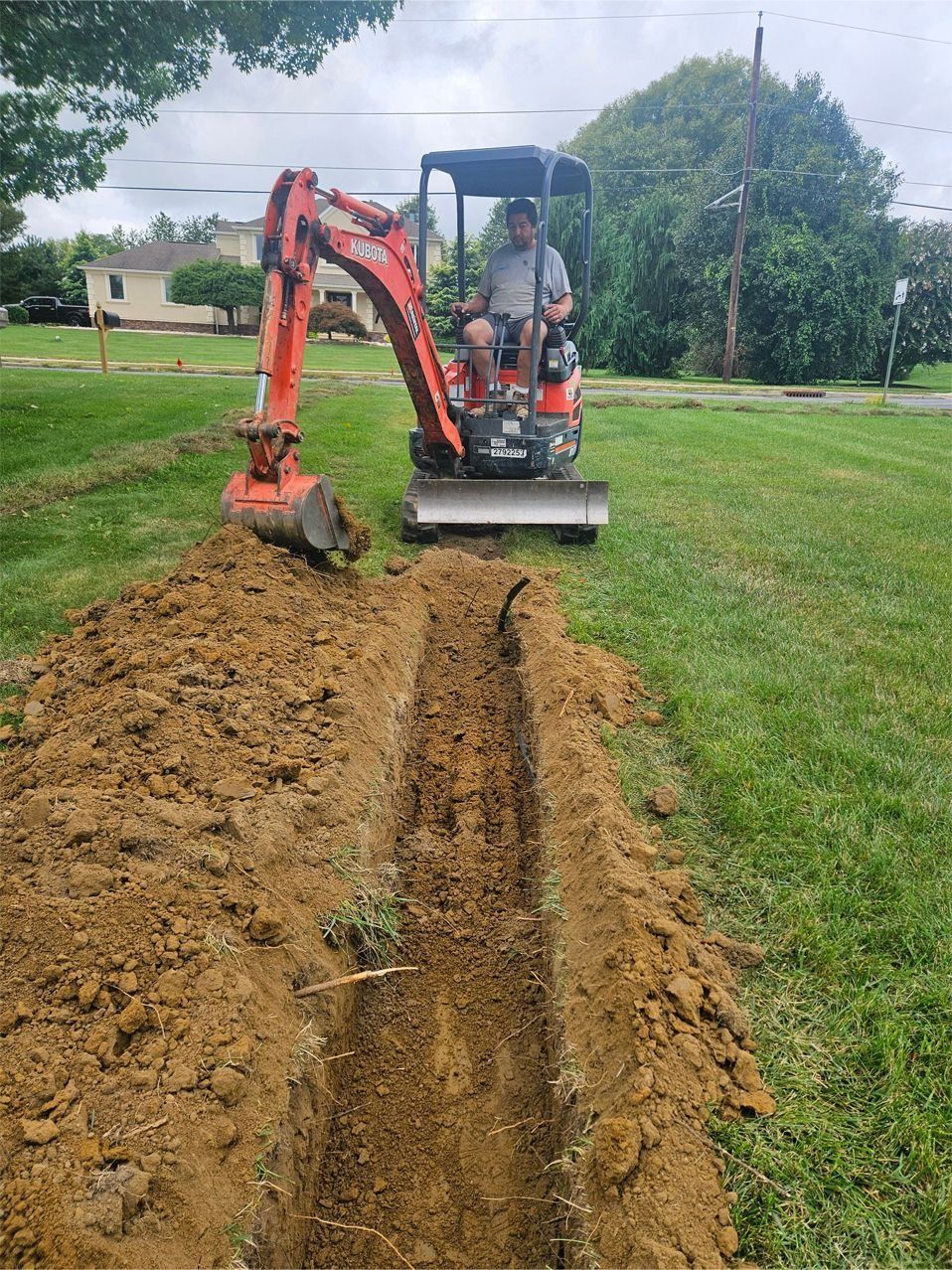An orange mini excavator digging a trench in a grassy yard.