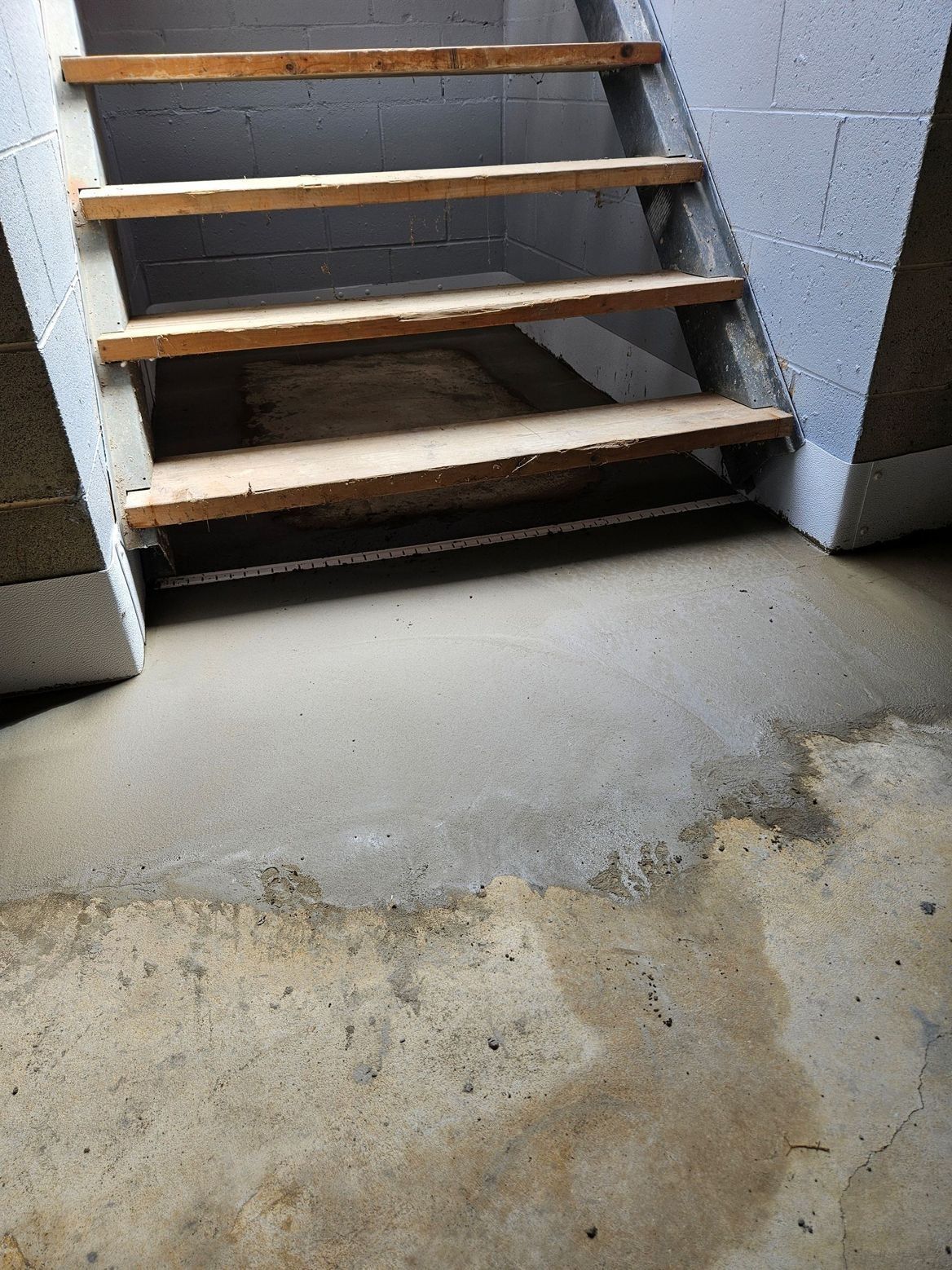 Wooden stairs descend into a basement area with concrete walls and a gray concrete floor.