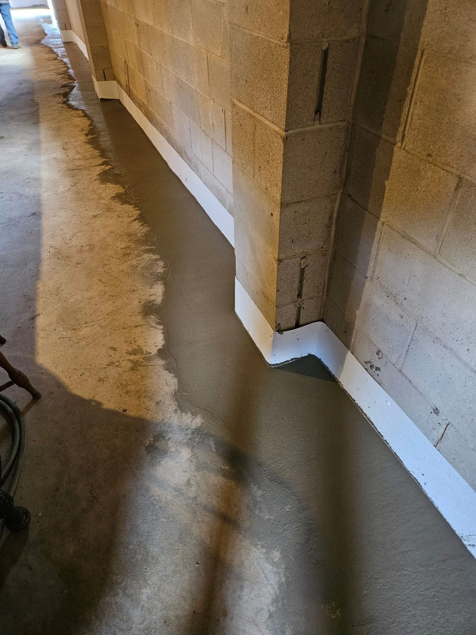 A concrete floor corner with a fresh white sealant line applied along the base of the block wall.