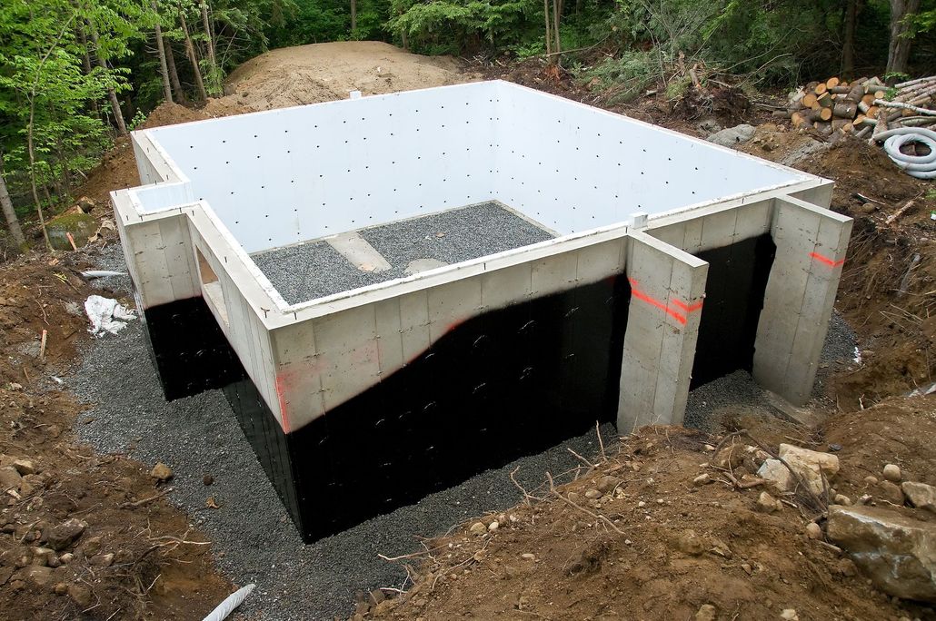 Concrete foundation with white insulated walls and dark interior, under construction in a wooded area.