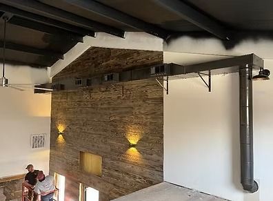 Interior with exposed brick wall, white upper walls, dark ceiling beams, and two wall sconces.